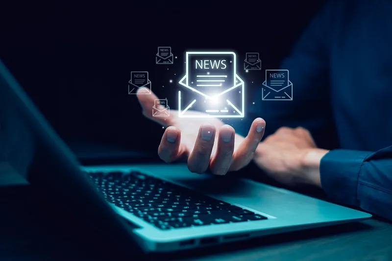 Person holding an envelope with a newsletter graphic over a laptop